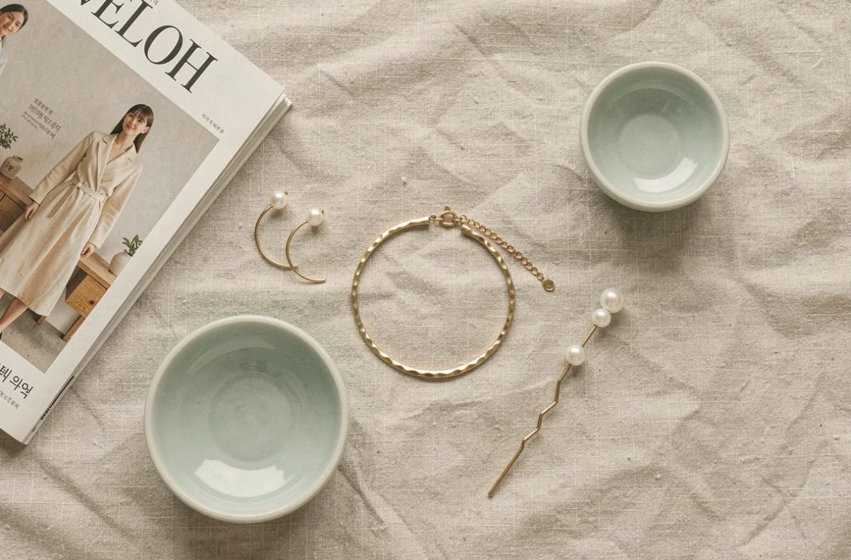 Bijoux coréens minimalistes disposés en flat-lay sur du lin avec magazine de mode coréen